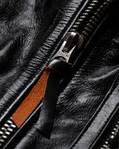 Close-up of a silver TALON zipper on crinkled black leather, with a black and tan leather pull.