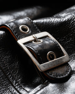 Close-up of a silver buckle and black leather strap detail on a jacket.